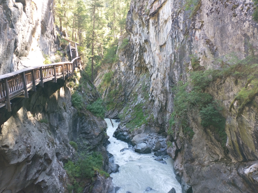 A wooden walkway suspended over a river extends into the canyon